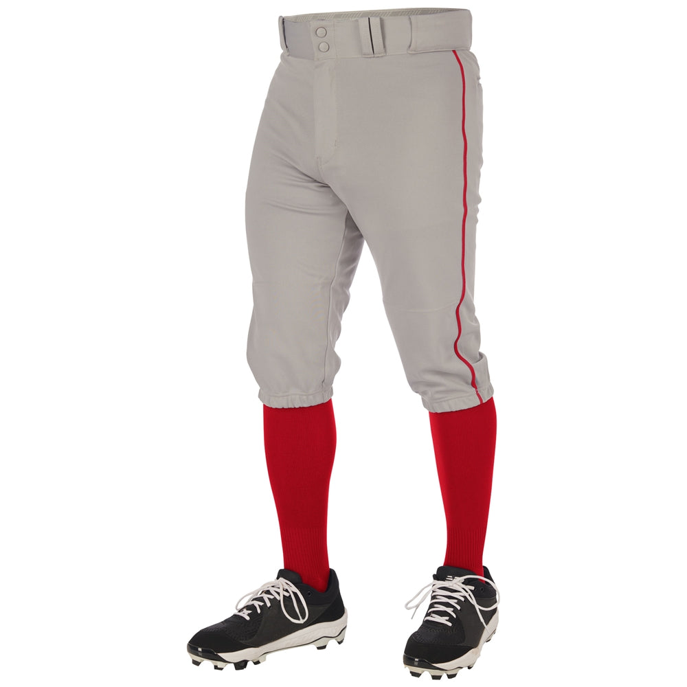 A person wearing Champro Sports Youth Triple Crown 2.0 Knicker Baseball Pants with red piping (BP70Y), paired with red knee-high socks, black and white cleats, and a matching gray belt, shown from the waist down.