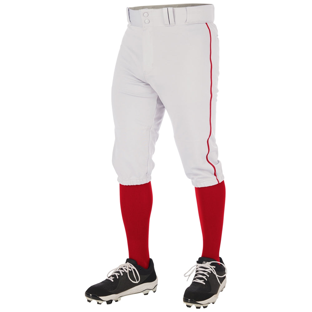 A person wears Champro Sports Youth Triple Crown 2.0 Knicker Baseball Pants with red piping (BP70Y), paired with red knee-high socks, a white belt, and black cleats, shown waist-down on a white background.