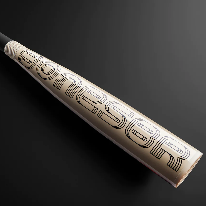 A close-up view of a baseball bat with a sleek, metallic finish and bold, stylized black geometric lettering along the barrel, resting on a dark, gradient background.