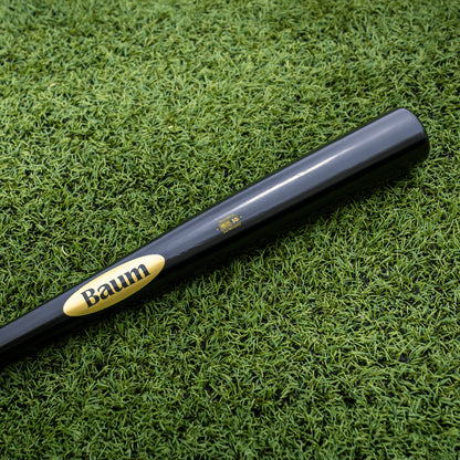 A Baum Gold Stock AAA Pro Balanced Composite Wood Bat: BBM, featuring the iconic yellow Baum logo and expertly handcrafted in the USA for elite performance, rests on bright green artificial turf.