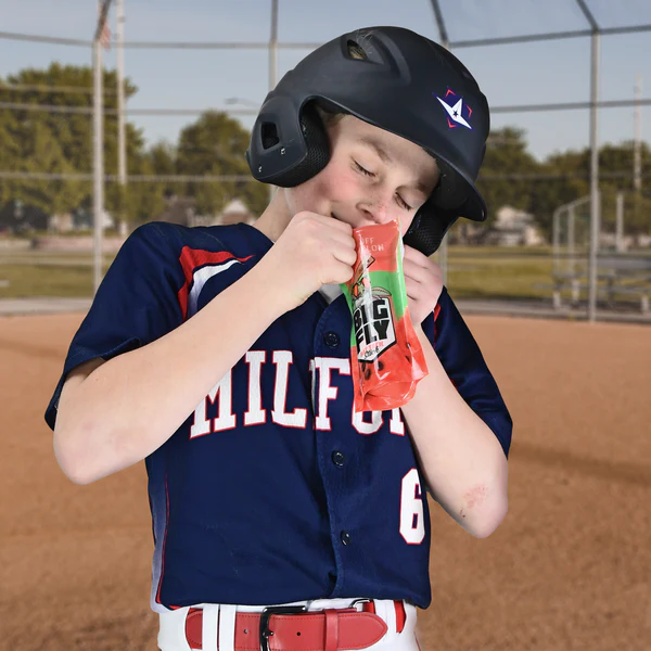 A young All-Star baseball player in a navy blue Milford jersey and black helmet stands on the field, gripping his bat with the All Star Big Fly Bat Tack Stick (BFST1) for better control as he prepares for the next pitch.