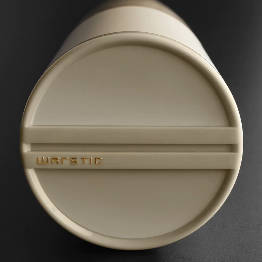 A close-up of the beige lid of a cylindrical container, with the word WARSTIC embossed in gold letters on the top against a dark background.