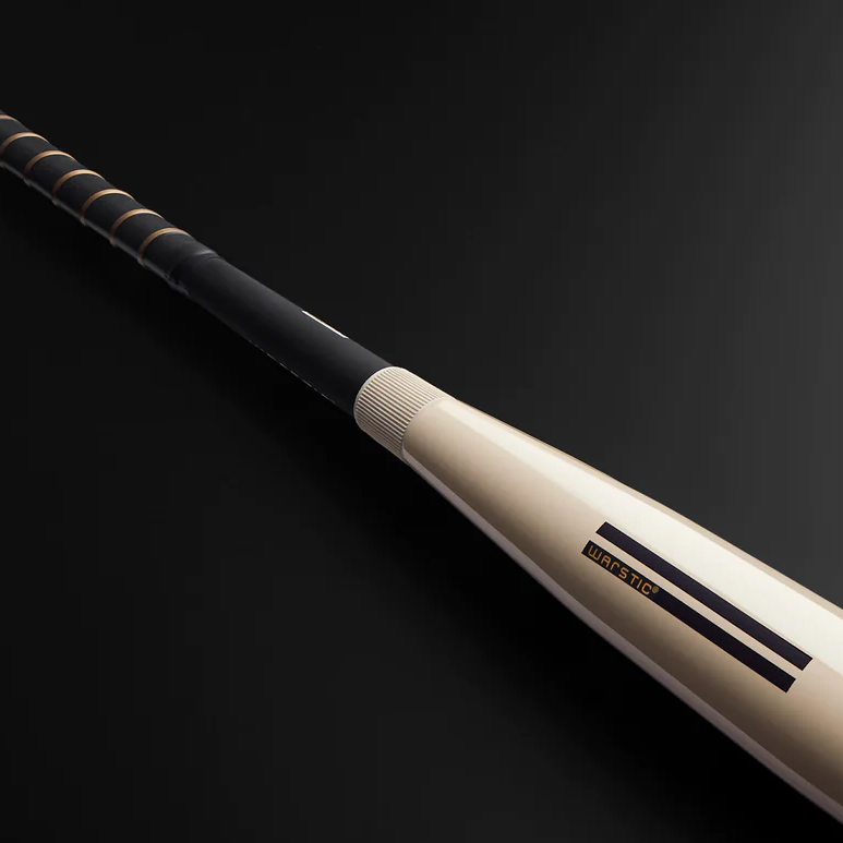 A close-up of a beige and black baseball bat with the brand name Warstic on the barrel, displayed on a dark background.