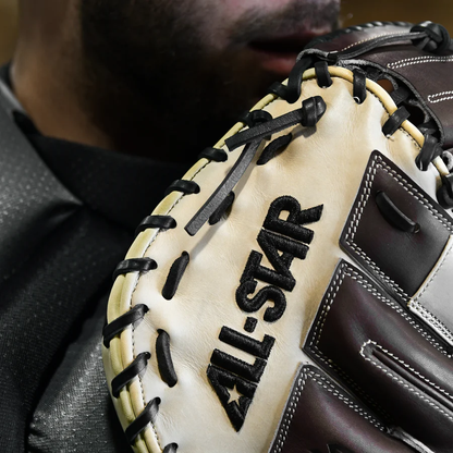 A close-up shows a person in a dark uniform holding the All Star S7 Elite 34" Baseball Catcher's Mitt: CM5000, with "ALL-STAR" embroidered in black and the lower part of their face visible behind the premium-grade rawhide glove.