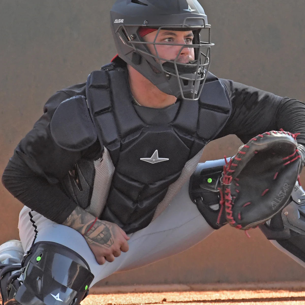 A man in a baseball uniform and helmet wears an SEI Certified All Star MVP Pro Catcher's Chest Protector: CPCC-5, which meets the NOCSAE standard.