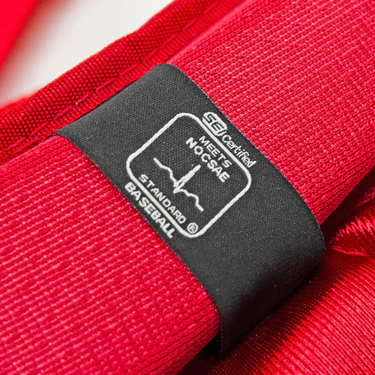 Close-up of a red strap with a black label that reads SEI Certified, Meets NOCSAE Standard, Baseball along with a heartbeat line graphic.