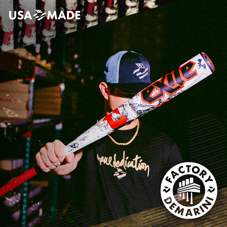 A person wearing a Brave Dedication shirt and baseball cap holds a DeMarini Voodoo One bat toward the camera. USA Made and Factory DeMarini logos are in the image corners.