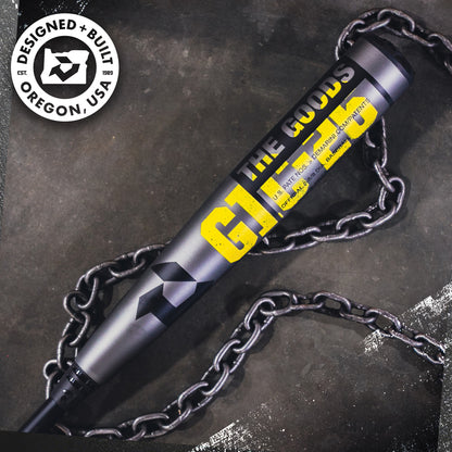 A DeMarini The Goods Gunmetal (-3) BBCOR Baseball Bat (WBD2650010) rests on a chain, featuring a black-and-white circular badge in the top left that reads DESIGNED + BUILT OREGON, USA.