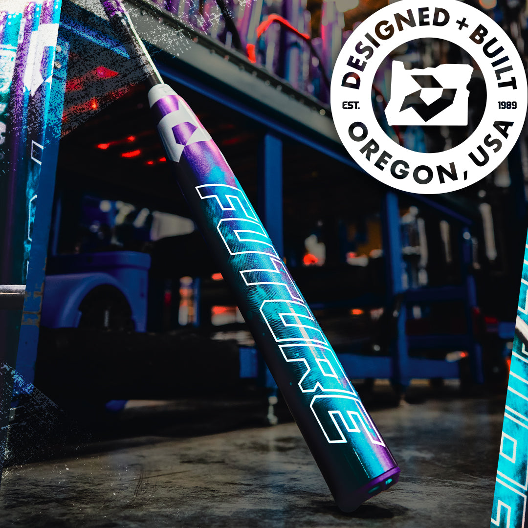A vibrant 2026 DeMarini Future (-10) Fastpitch Softball Bat: WBD2674010 stands upright in a workshop, featuring a bold FUTURE graphic. A circular logo at the top right reads DESIGNED + BUILT OREGON, USA with EST. 1989 and a stylized emblem.