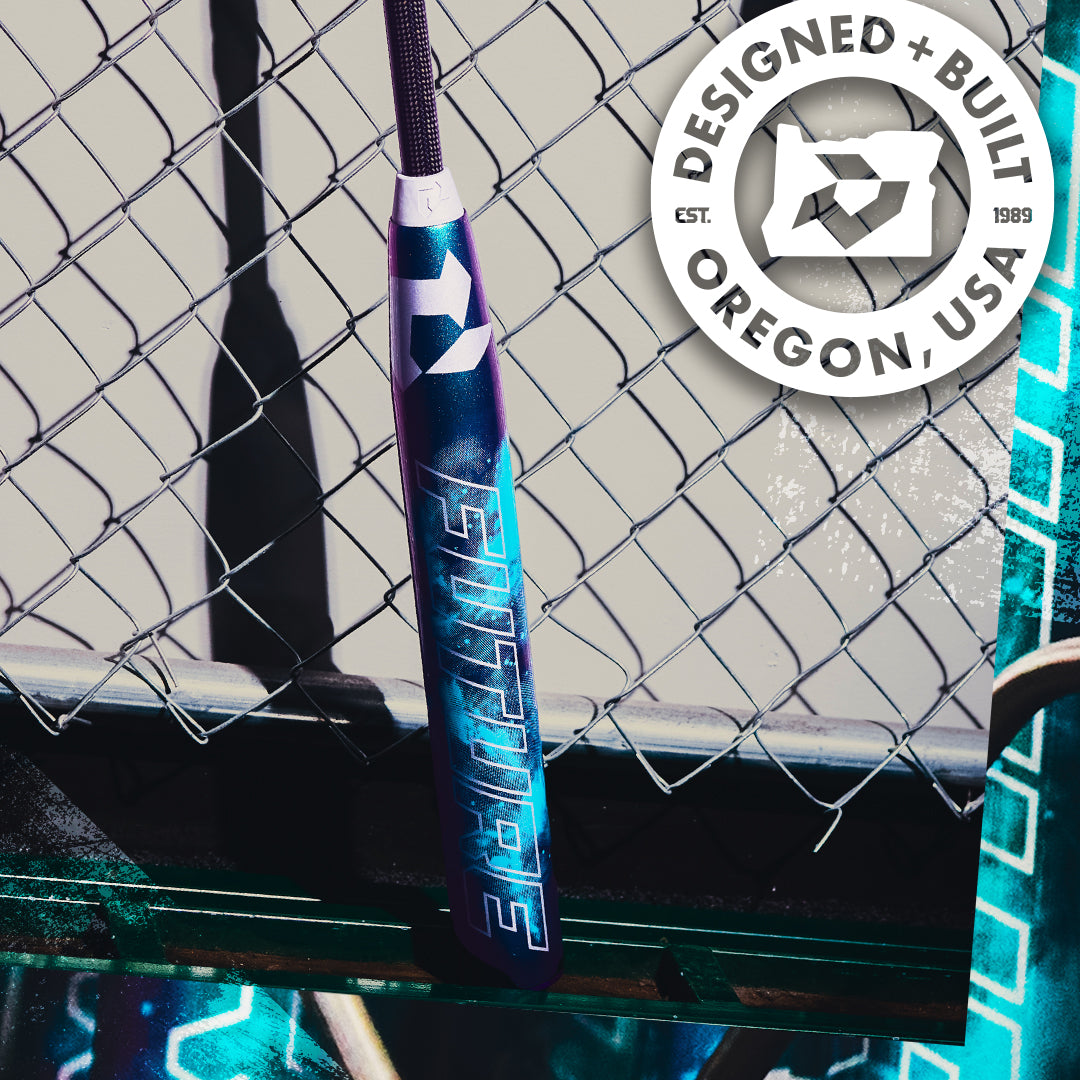A blue and purple 2026 DeMarini Future (-10) Fastpitch Softball Bat (WBD2674010) with "Future" leans on a chain-link fence. A circular logo reads "Designed + Built Oregon, USA, Est. 1989." This DeMarini bat offers a large sweet spot.