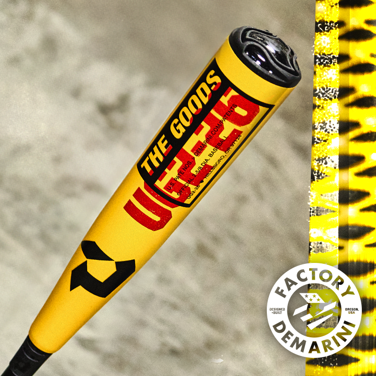 A close-up of a yellow DeMarini baseball bat labeled THE GOODS with black and red accents. A circular FACTORY DEMARINI logo appears in the bottom right corner against a blurred background.