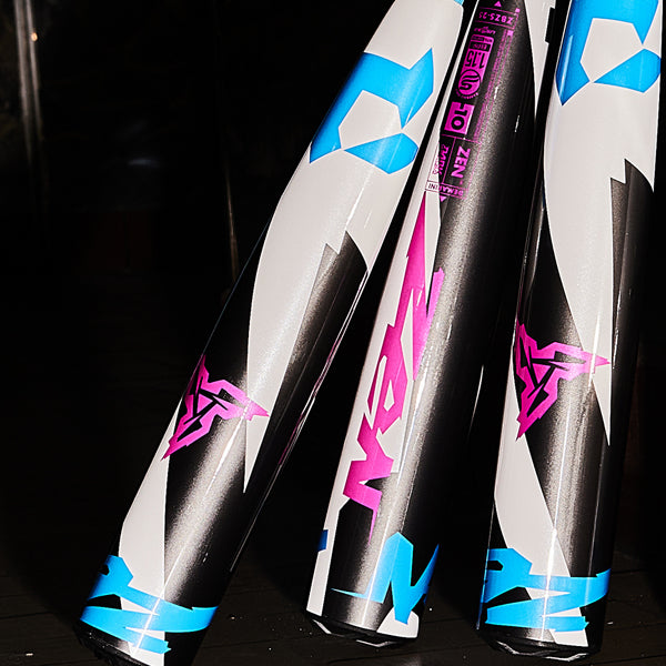 Three metallic baseball bats with bold blue, pink, black, and white graphics, including stylized logos and text, are standing upright against a dark background.