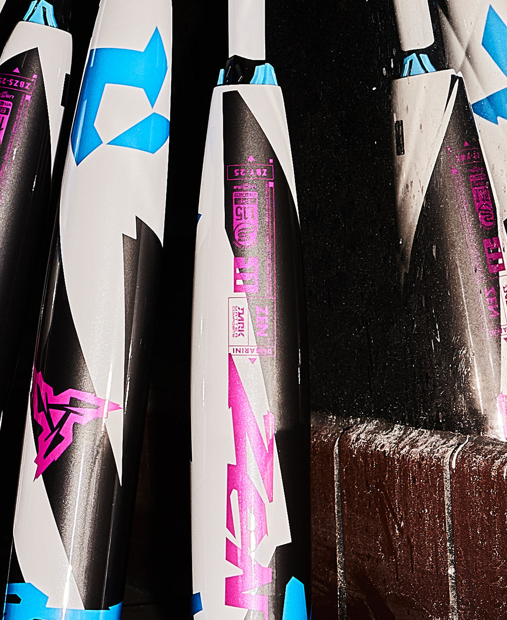 Close-up of several USSSA bats, including the 2025 DeMarini ZEN (-10) 2 3/4" from DeMarini, with bold white, blue, black, and pink geometric designs. Some display pink logos on a dark background and feature Dark Matter Composite technology.