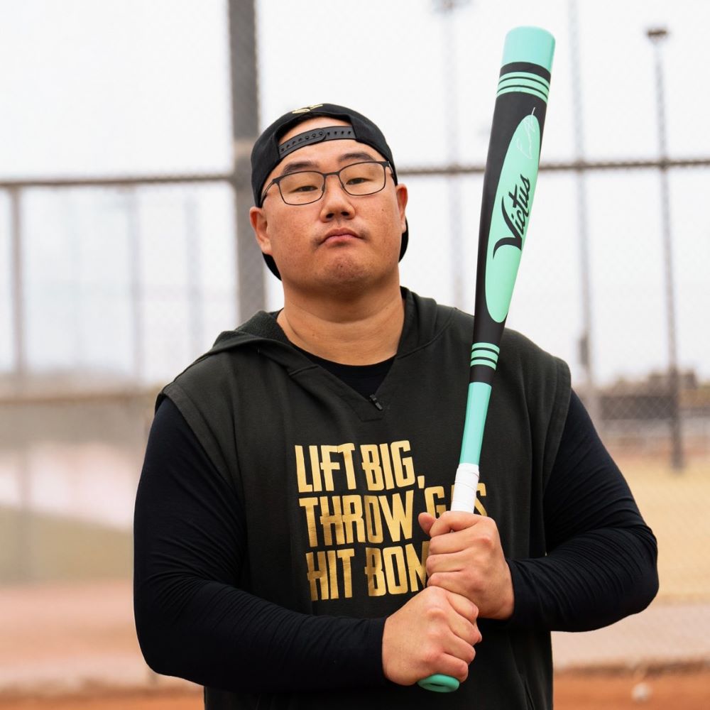 A man holding the 2025 Victus Vibe Pro-Crayon King of Juco (-3) BBCOR Baseball Bat (VCBVIBC-KJ), an aluminum bat by Victus featuring a vibration reducing knob.