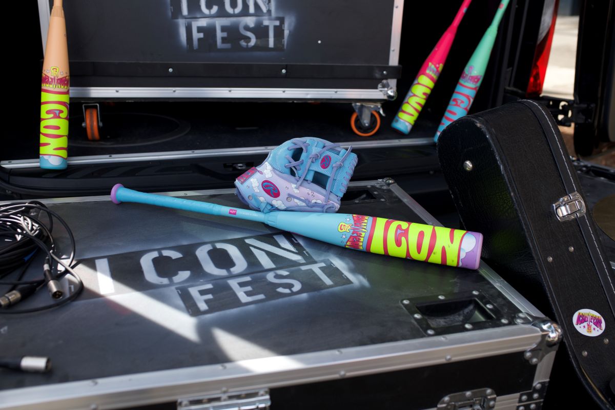 A blue and purple glove and a colorful 2026 Rawlings Icon Fest (-10) USSSA Baseball Bat (RUT6IFL10) sit on a black ICON FEST case, with extra bats and a limited edition guitar case nearby.