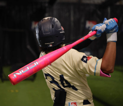 Wearing a helmet and cream jersey with #34, a baseball player swings the Rawlings 2025 Icon Electric Unicorn (-3) BBCOR Bat (RBB5IPK3) in an indoor facility, with blue gloves and arm sleeves completing the look.