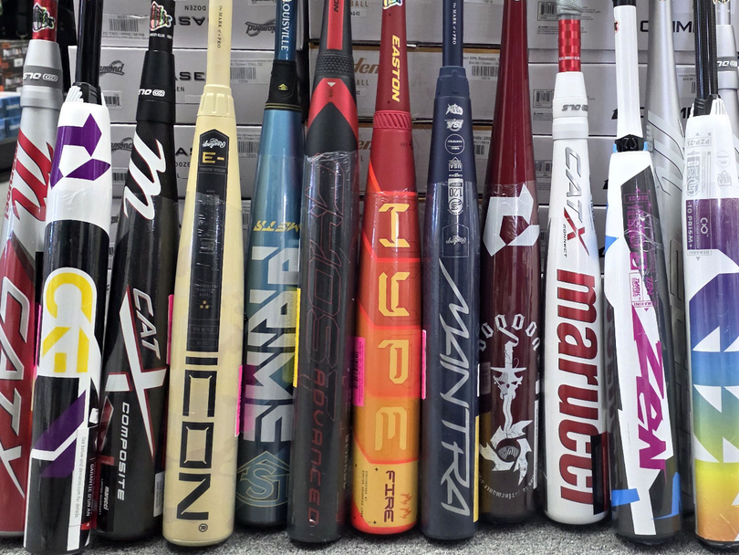 Assorted baseball and softball bats of various brands and colors are displayed upright in a row, showing logos and names like CAT, ICON, PRIME, HYPE, MANTRA, Marucci, and ZEN.