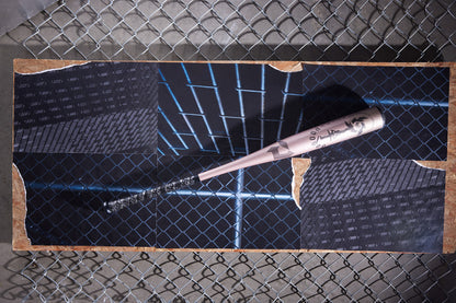 A pink eyeliner pen lies diagonally on vibrant photos of blue-lit chain-link fences and brick walls, set atop a wooden board—echoing the sleek, modern design of the DeMarini 2025 Voodoo One Rose Gold (-3) BBCOR Baseball Bat: WBD2628010.