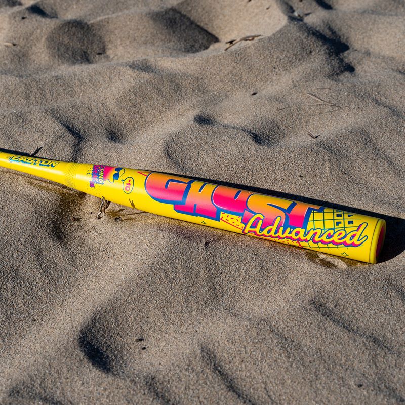 A 2026 Easton Ghost Advanced Spring Break Yellow (-10) Fastpitch Softball Bat (EFP6GHSY10) with Double Barrel construction and colorful graphics rests on sandy ground in bright sunlight.