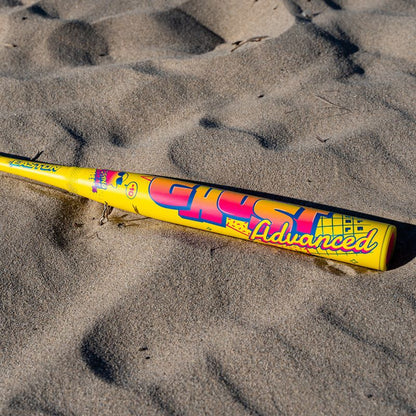 A 2026 Easton Ghost Advanced Spring Break Yellow (-10) Fastpitch Softball Bat (EFP6GHSY10) with Double Barrel construction and colorful graphics rests on sandy ground in bright sunlight.