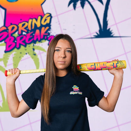 A young woman with straight brown hair holds the 2026 Easton Ghost Advanced Spring Break Yellow (-11) Fastpitch Softball Bat (EFP6GHSY11) over her shoulders, standing before a vibrant Spring Break sign and palm trees on a pink grid background.