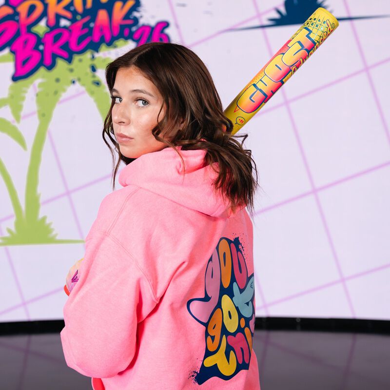 A teenage girl in a bright pink “You Got This” hoodie holds an Easton 2026 Ghost Advanced Spring Break Yellow (-10) Fastpitch Softball Bat (EFP6GHSY10) over her shoulder, standing indoors against a Spring Break 26 backdrop.