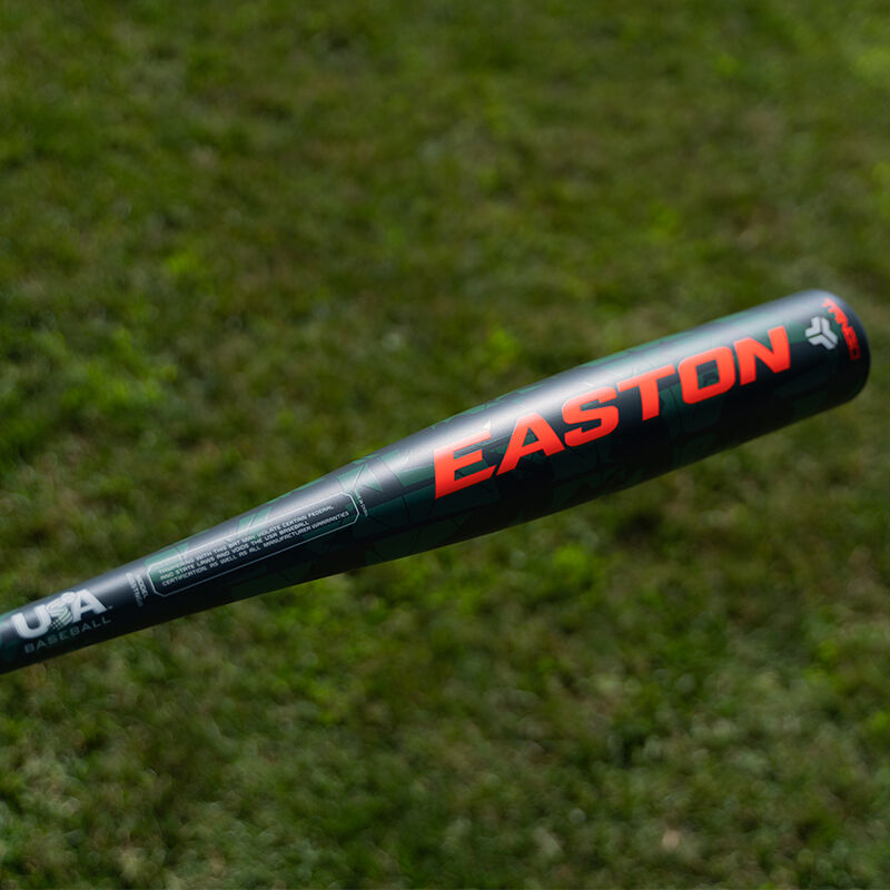 A black 2025 Easton Tango (-8) USA Baseball Bat (EUS5TNG8) with red lettering is held over a grassy field; “USA Baseball” in white is shown near the handle.