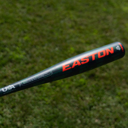 A black 2025 Easton Tango (-8) USA Baseball Bat (EUS5TNG8) with red lettering is held over a grassy field; “USA Baseball” in white is shown near the handle.