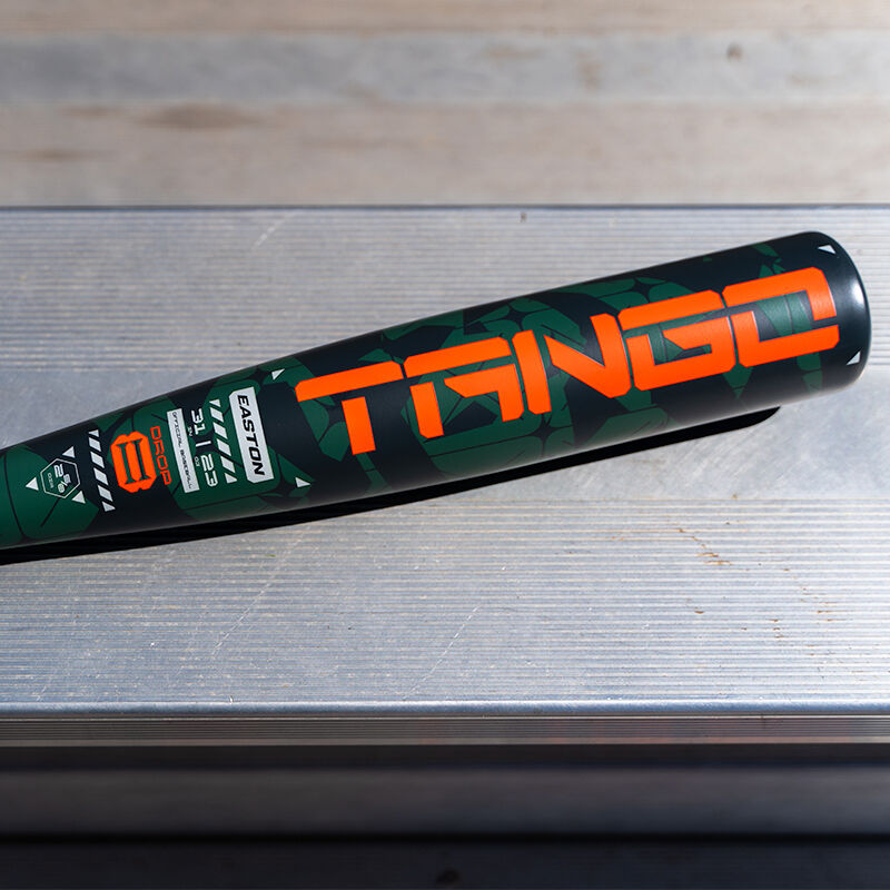A close-up of the 2025 Easton Tango (-8) 2 5/8" USA Baseball Bat (EUS5TNG8), a black and green youth bat with bold orange "TANGO" lettering and various logos, lies on a metallic surface.