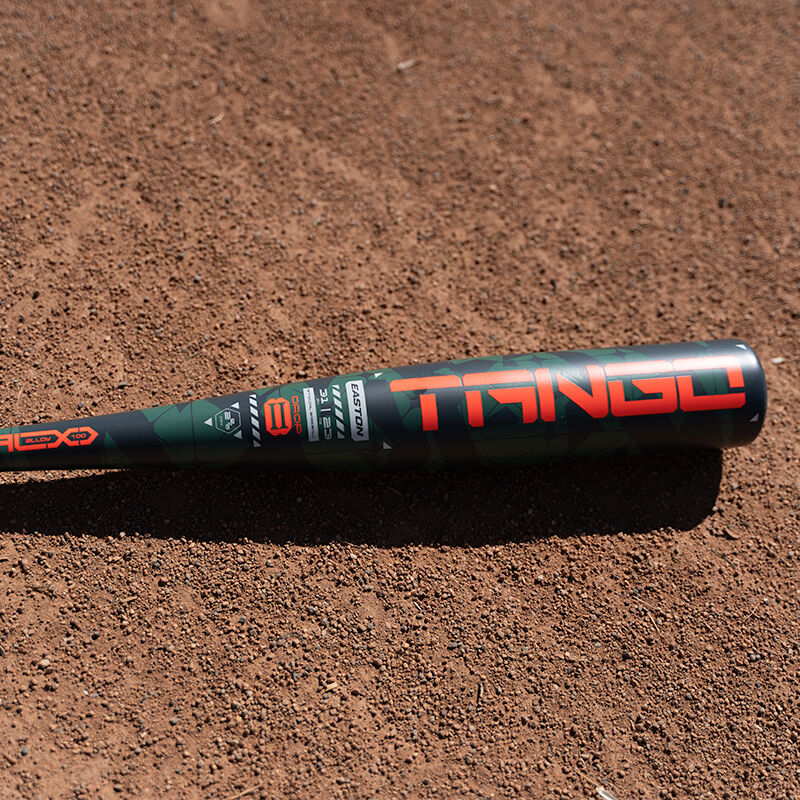 A close-up of the Easton 2025 Tango (-8) 2 5/8" USA Baseball Bat, black and red, labeled "Tango," lying on a dirt baseball field.
