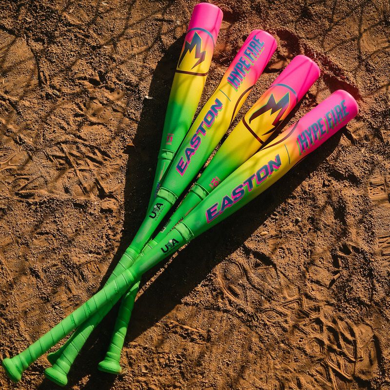 Three vibrant baseball bats with green and pink gradients, including the 2026 Easton Hype Fire (-11) USA Baseball Bat by Easton, labeled EASTON and HYPE FIRE, lie crossed on a dirt field—ideal for players seeking a new bat for 2026.