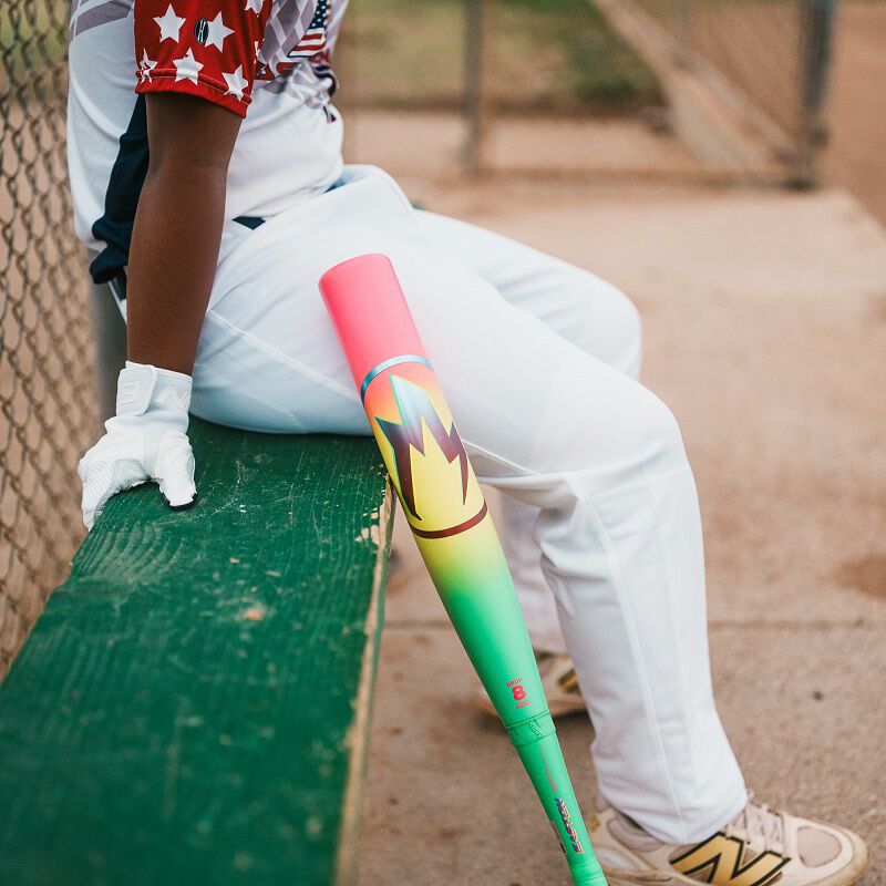 A baseball player in white pants and a star-patterned jersey sits on a green bench, holding an Easton 2026 Hype Fire (-11) 2 5/8" USA Baseball Bat (EUS6HYP11). Only the lower half is visible. The bat is USA certified.