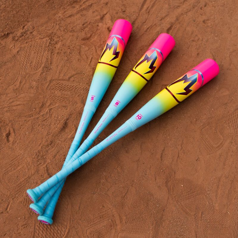 Three 2026 Easton Hype Fire (-8) USSSA Baseball Bats by Easton, featuring blue handles, yellow gradients, and pink ends with a bold crown design, are arranged parallel on a dirt field with handles at the bottom left.