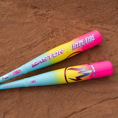 Two colorful bats with vibrant pink, yellow, and blue designs lie on reddish-brown dirt. One is the 2026 Easton Hype Fire (-8) 2 3/4" USSSA Baseball Bat: EUT6HYP8 by Easton, known for its advanced ThermoComposite technology.