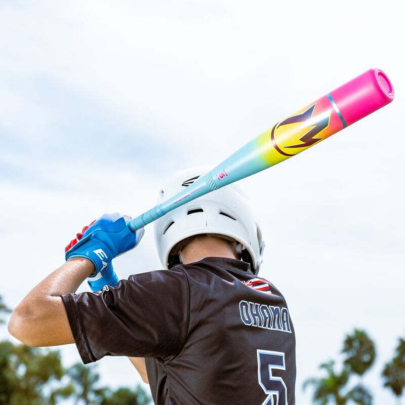 A baseball player in a white helmet and black OHANA #5 jersey gets ready to bat with the 2026 Easton Hype Fire (-5) 2 3/4" USSSA Baseball Bat (EUT6HYP5). Palm trees and sky create a vibrant background.