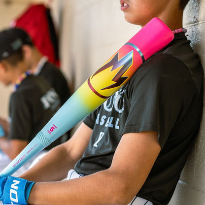 A baseball player in black jersey and white pants leans against a dugout wall, holding the 2026 Easton Hype Fire (-8) 2 3/4" USSSA Baseball Bat (EUT6HYP8) by Easton over his shoulder. Another player is visible in the blurred background.