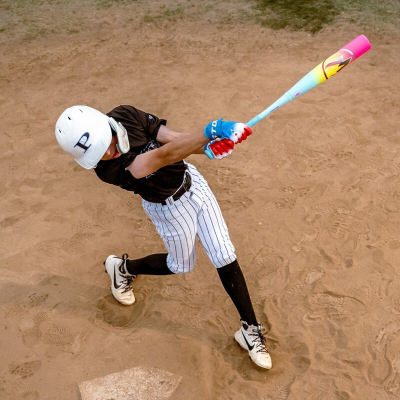 A baseball player in a white helmet and striped pants swings the 2026 Easton Hype Fire (-5) USSSA Baseball Bat (EUT6HYP5) at home plate on a sandy field, captured mid-swing from above.