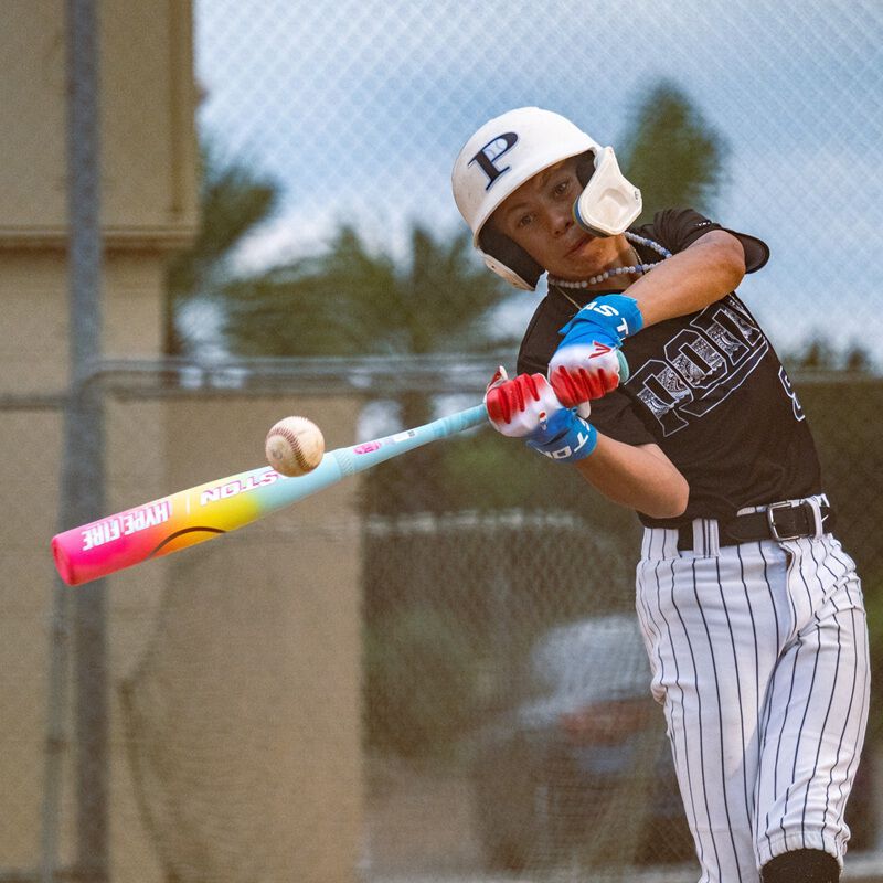A young baseball player in a black and white uniform swings the 2026 Easton Hype Fire (-5) 2 3/4" USSSA Baseball Bat (EUT6HYP5) on an outdoor field, wearing a white helmet and gloves.