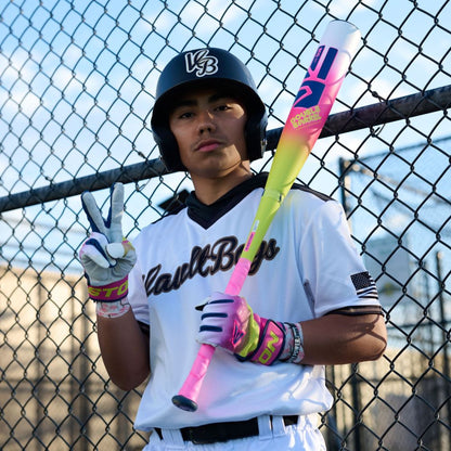 A young baseball player in uniform and helmet stands by a chain-link fence, making a peace sign with his gloved hand while holding the 2026 Easton Dub (-10) USSSA Baseball Bat: EUT6DUB10 as the sun sets.