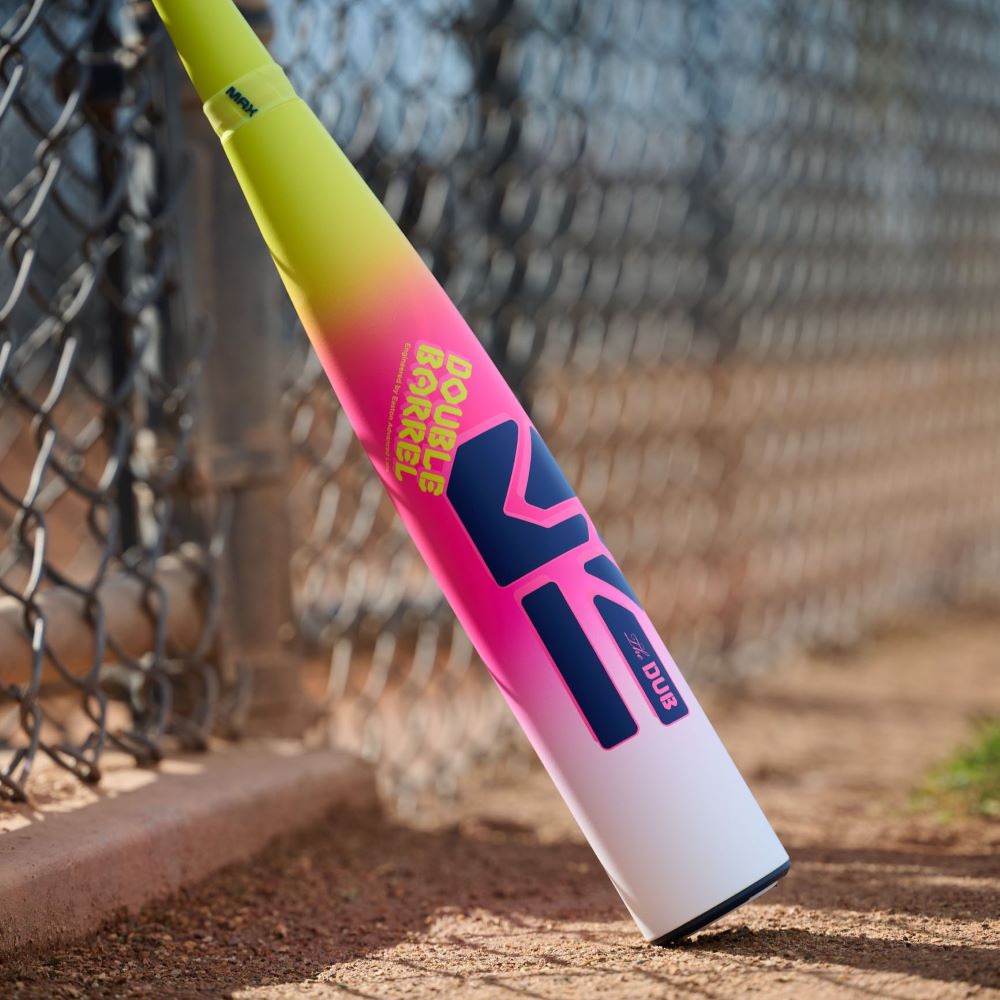 The Easton 2026 Dub (-10) USSSA Baseball Bat (EUT6DUB10), featuring a yellow, pink, and white gradient design and Double Barrel labeling, leans against a chain-link fence near a baseball field.