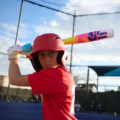 A young baseball player in a red shirt and helmet grips the 2026 Easton Dub (-10) 2 3/4" USSSA Baseball Bat: EUT6DUB10, ready to swing on an outdoor field with a blue sky and chain-link fence in the background.