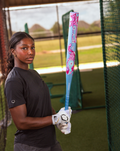 A woman wearing a black shirt and white gloves holds the Louisville Slugger Kryo One (-9) Fastpitch Softball Bat (2027, WBL4274010), standing in an outdoor batting cage.