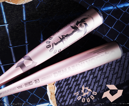 Two rose gold 2025 DeMarini Voodoo One (-3) BBCOR bats (WBD2628010) with X14 Alloy Barrels cross on a black chain-link surface, surrounded by wood shavings and the DeMarini logo in the foreground.
