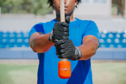 A person in black gloves and a blue shirt grips a bat with the orange Hitting Knob Bat Weight by Hitting Knob, standing on a field with empty stadium seats to help improve bat speed.