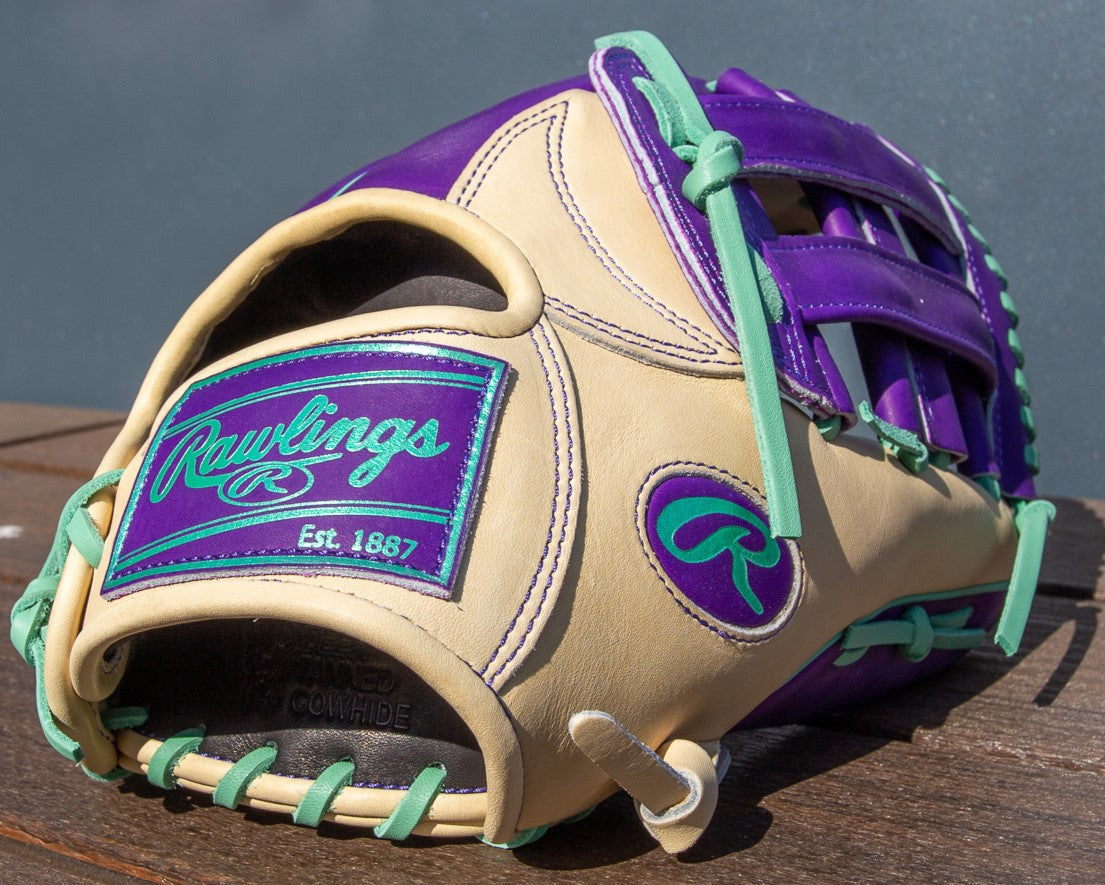 A Rawlings Heart of the Hide 12.75" Color Sync (PROR3039-6CPU) glove, tan with purple and teal accents, lies on a wooden surface. A large teal patch displays the Rawlings logo and Est. 1887.