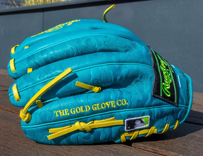 A vibrant teal Rawlings Heart of the Hide 12" Color Sync Baseball Glove (PROR206CFB-11TE) with yellow laces, embossed patterns, THE GOLD GLOVE CO., and an MLB logo in yellow rests on a wooden surface.