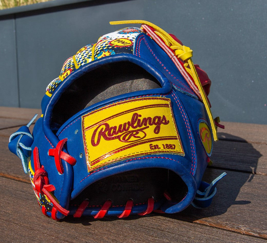 A Rawlings Heart of the Hide 12.75" Color Sync Baseball Glove (PROR3039-6RSS) with blue, yellow, red, and white accents sits on a wooden surface in sunlight. The Rawlings logo and "Est. 1887" appear on a yellow patch.