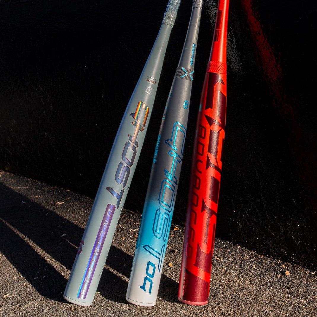 Three vibrant Easton Ghost Advanced (-8) Fastpitch Softball Bats (EFP6GHAD8)—in silver-purple, silver-blue, and red—lean against a black wall on sunlit concrete, highlighting the Double Barrel construction.