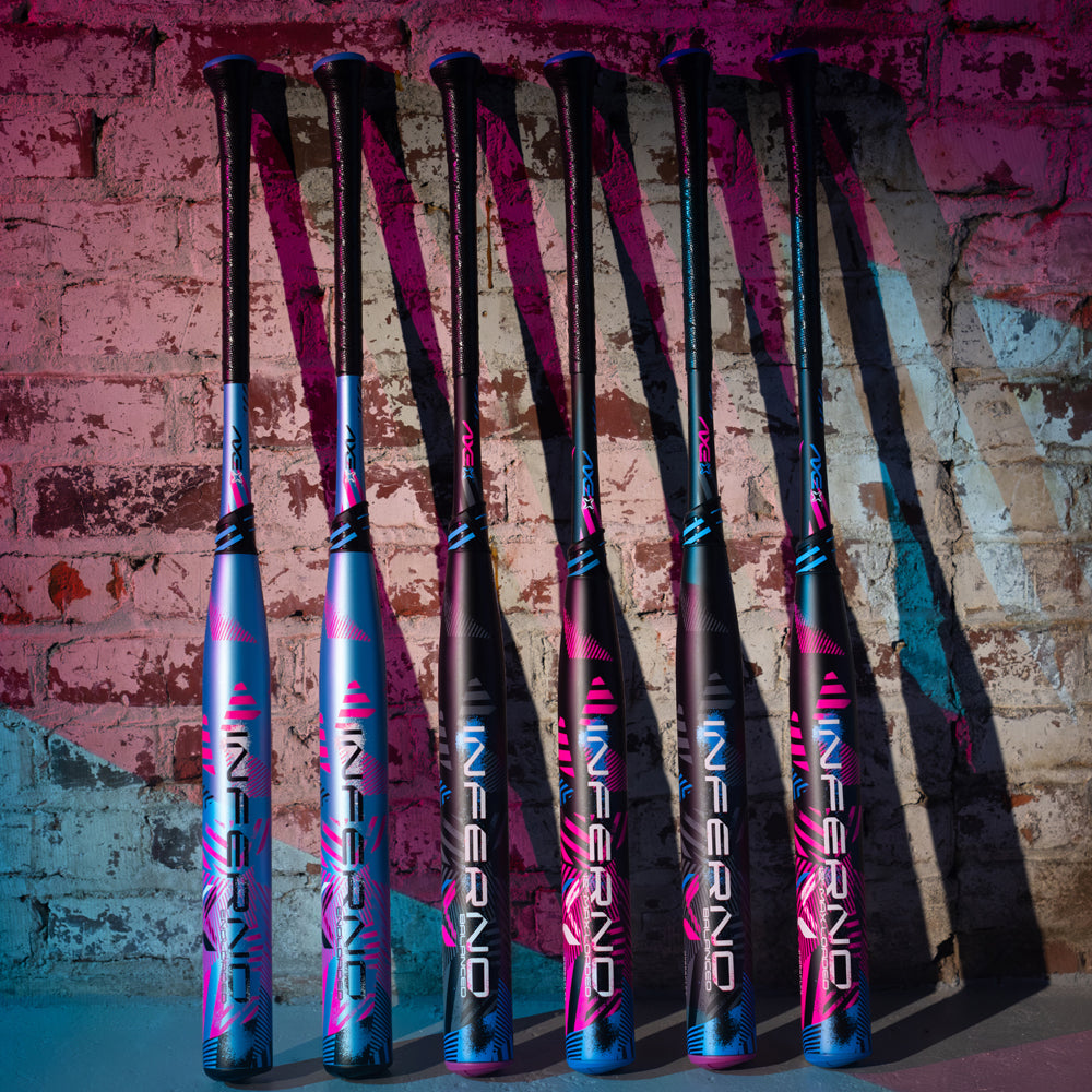 Six vibrant 2024 AXE Inferno Balanced NSA USSSA Slowpitch Softball Bats (L154M-FLR) with bold blue and pink designs stand upright against a painted brick wall, showcasing AXE’s advanced Hyperflex Barrel Technology under dramatic lighting.