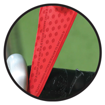 Close-up of a red flag with small textured dots and text, held by a metallic clamp or clip against a blurred green background.